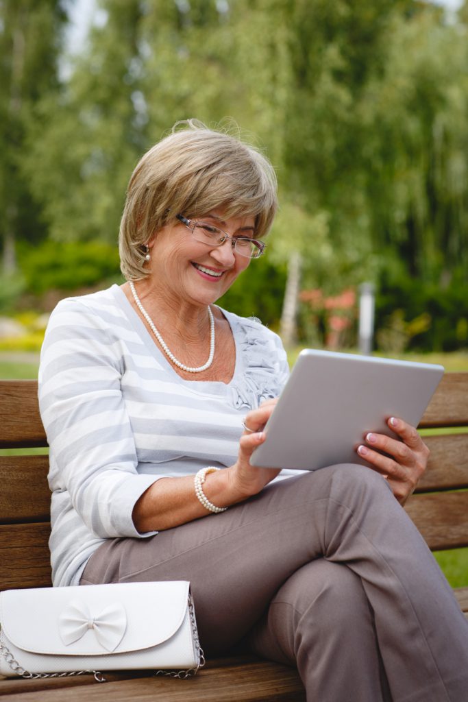 A woman sitting on top of a bench using her tablet.